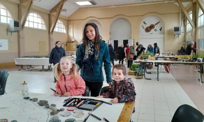 Laure et son stand de peinture sur galets à la Fête du Printemps du collectif Tiers-lieu en Magnoac, avec deux petites artistes, Rose et Olivia.