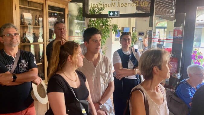 Avec ses lunettes sur la tête Victoria au fond de la salle, écoute le discours du maire