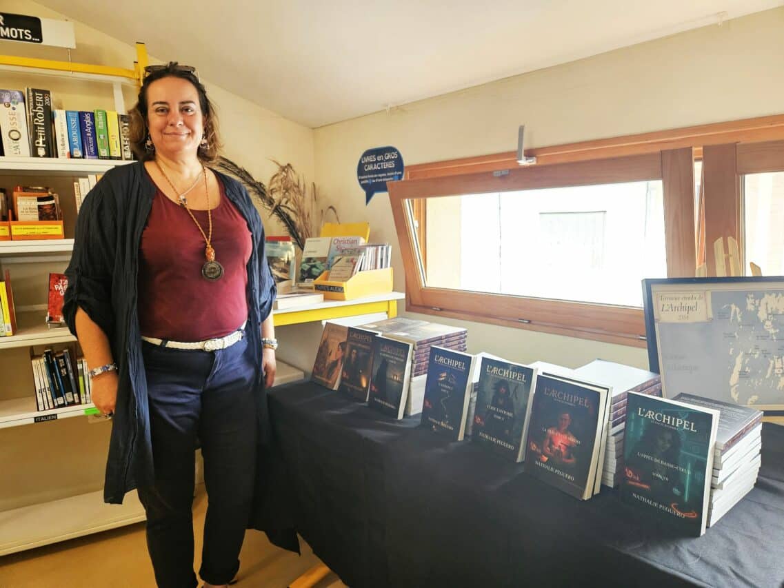 Nathalie Peguero et les 7 tomes publiés de la saga l'Archipel qui en compte 13, en séance de dédicace à la médiathèque de l'Isle en Dodon.